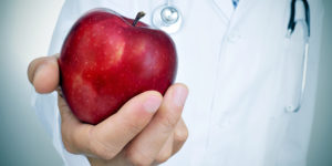 Closeup of a young caucasian doctor with a red apple in his hand, depicting the idea of the healthy eating  as a basis for a good health