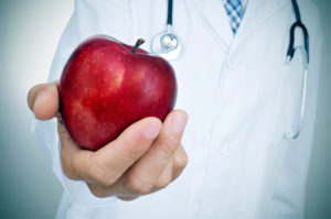 closeup of a young caucasian doctor with a red apple in his hand, depicting the idea of the healthy eating  as a basis for a good health
